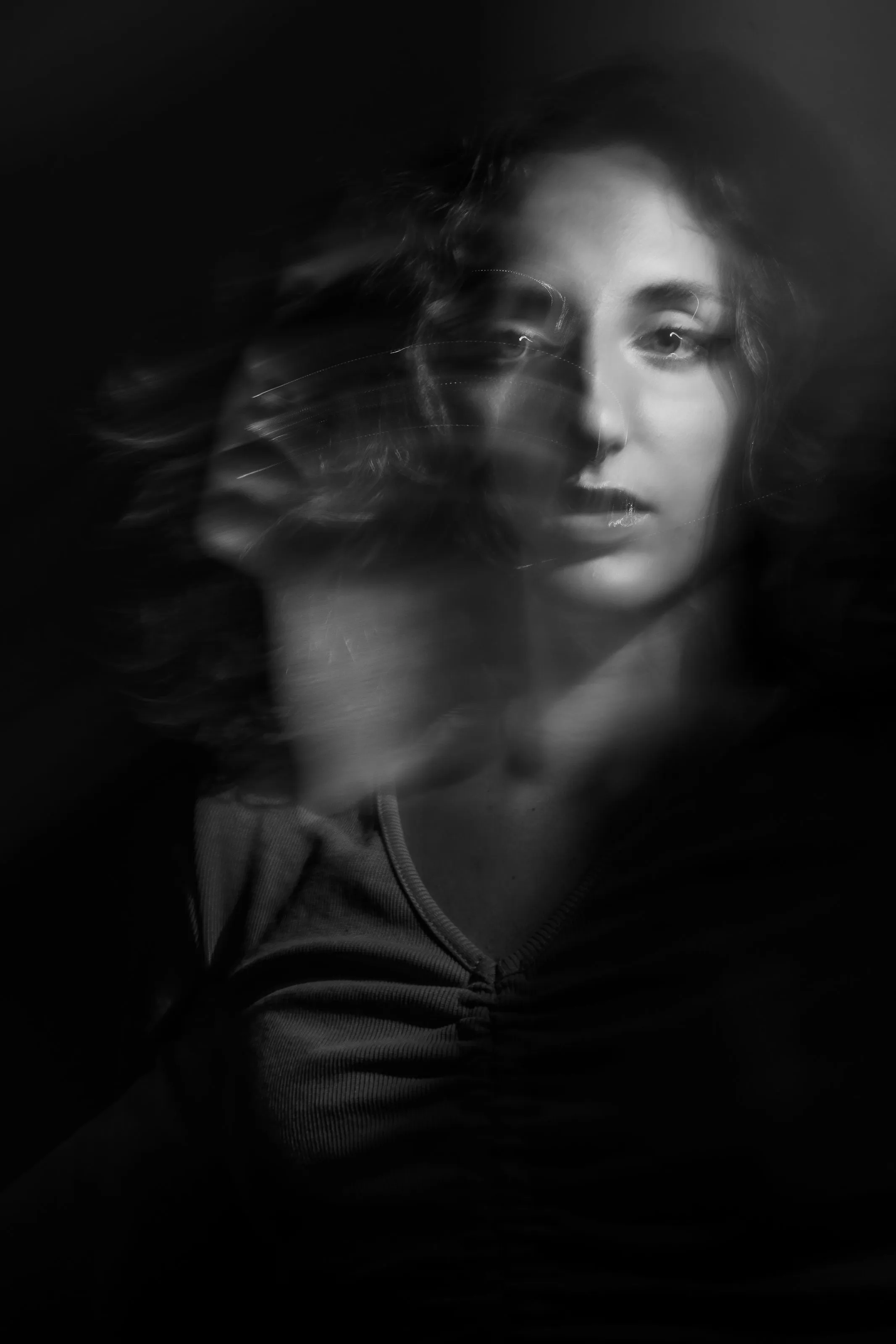 A black and white portrait of a woman with motion blur across her face and hair, from a long exposure or camera movement during the shot