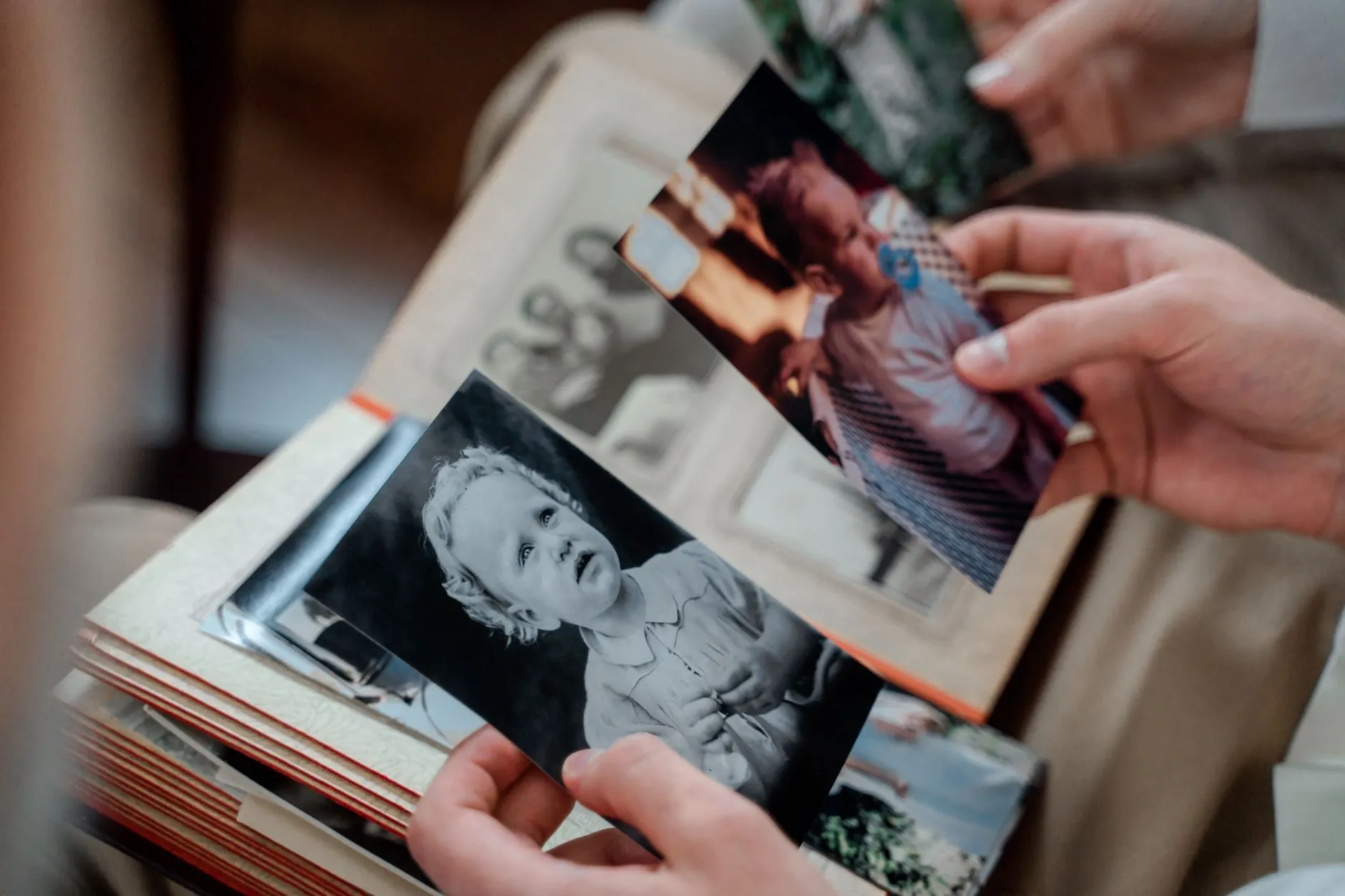 Two hands holding old family photo prints, pulling them out of a photo album to look closer