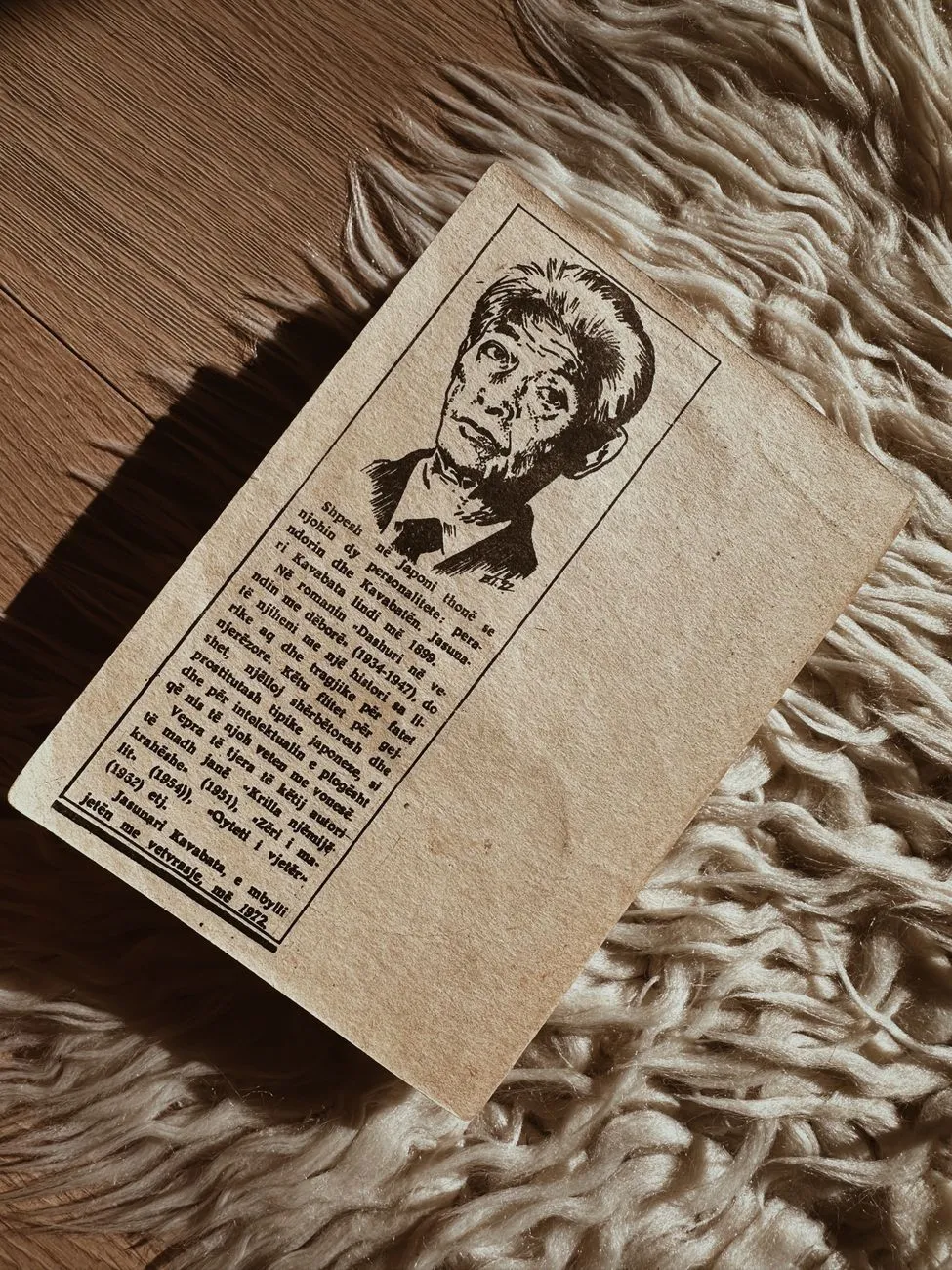 A small vintage newspaper clipping with a printed halftone portrait, lying on a woven rug