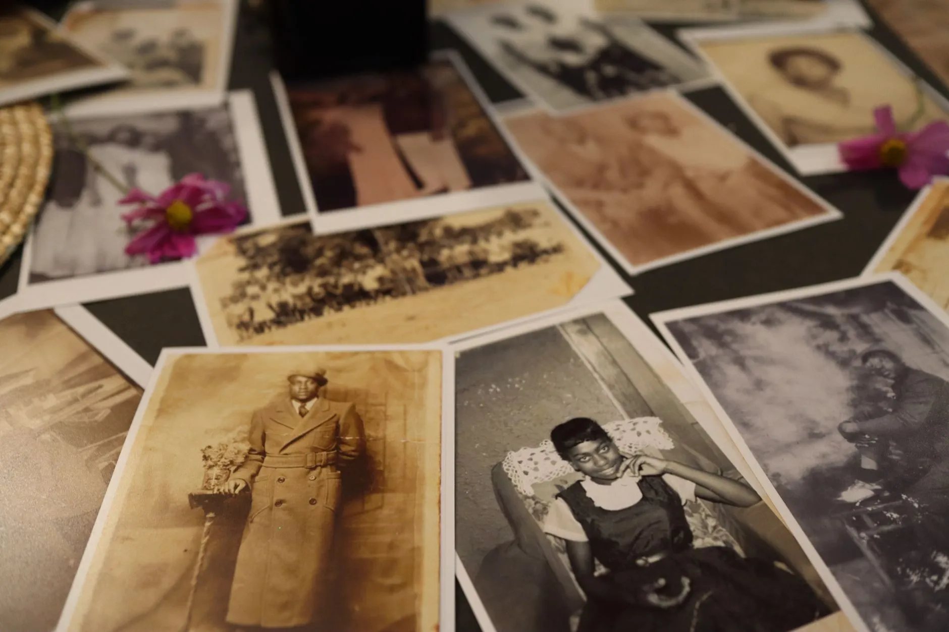 A spread of overlapping vintage sepia and black and white photographs on a table, some faded and some sharp, photographed at a low angle